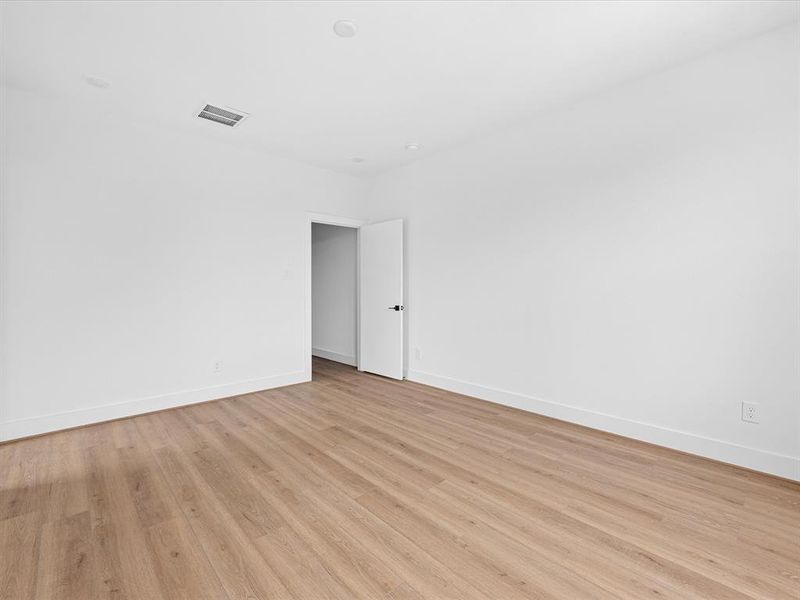 This photo shows a bright, empty room with clean white walls and light hardwood flooring. It features recessed lighting and a white door, creating a modern and spacious atmosphere ideal for personalization.