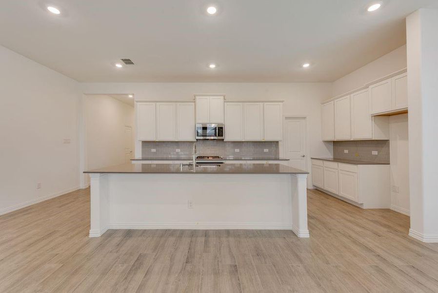 Kitchen featuring light hardwood / wood-style flooring, decorative backsplash, white cabinets, and a kitchen island with sink