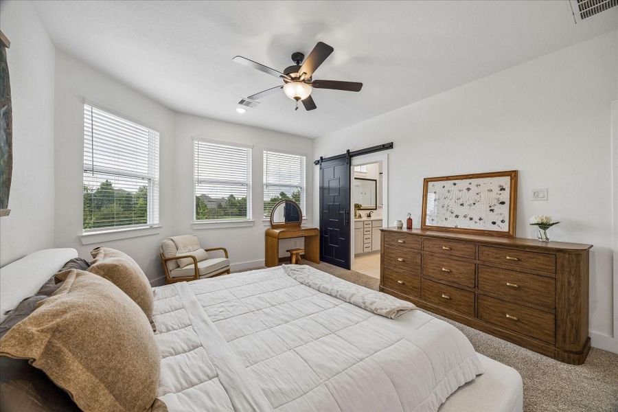 The well-appointed primary bedroom is filled with natural light from a wall of windows and features soaring ceilings and a beautifully ornate sliding door for a refined finishing touch.