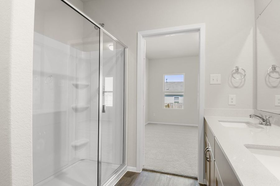 Image of a primary bathroom with a white walk-in shower, a large white vanity and a door leading to the bedroom