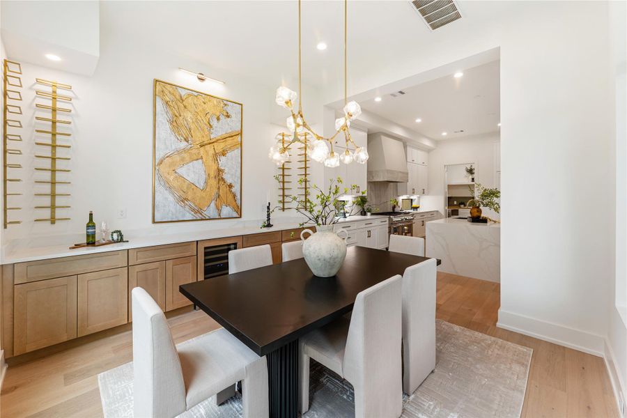 Elegant dining room features a stunning built-in wine display holding 48 bottles, perfectly complemented by a premium Thermador wine refrigerator.  Expansive wall provides a stunning backdrop for art display, featuring a distinctive black and gold art lighting fixture.