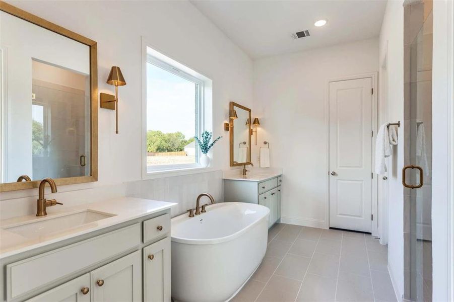 Bathroom featuring a shower stall, a freestanding tub, light tile patterned floors, two vanities, and recessed lighting
