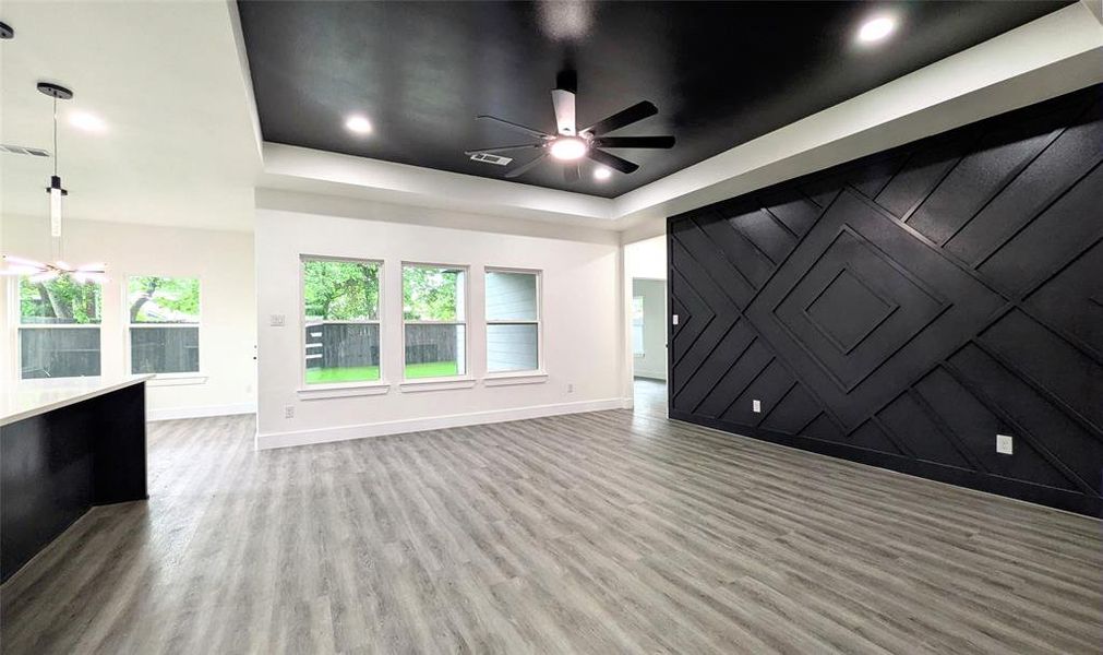 Unfurnished living room featuring ceiling fan, baseboards, a raised ceiling, and wood finished floors