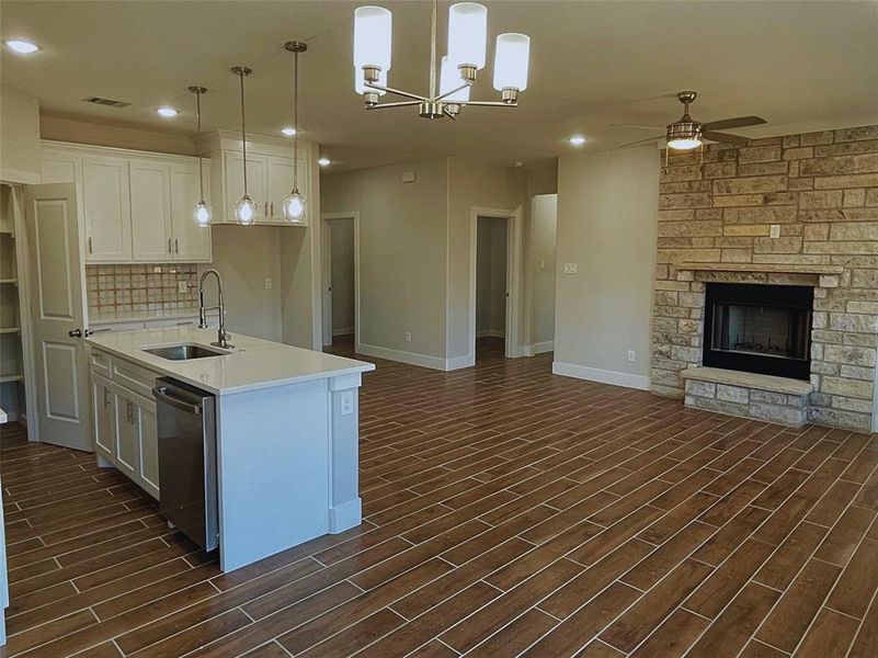 Kitchen featuring sink, dishwasher, white cabinetry, a fireplace, and decorative light fixtures