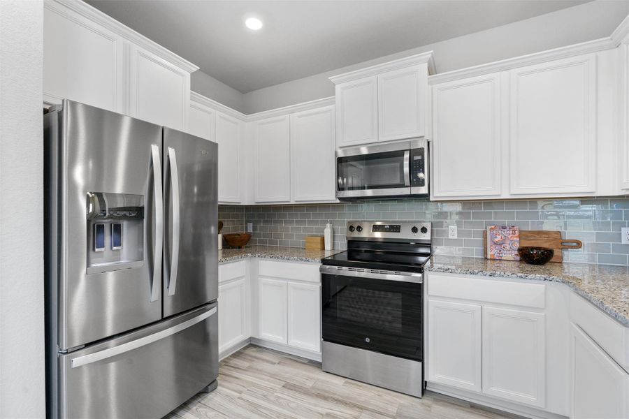 Kitchen with appliances with stainless steel finishes, white cabinets, light stone countertops, backsplash, and light wood-type flooring
