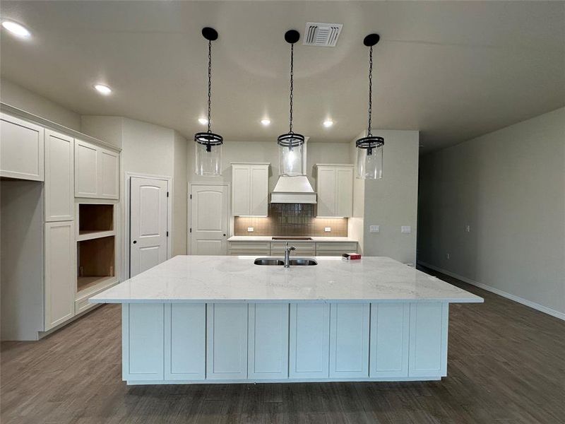 Kitchen featuring light stone counters, tasteful backsplash, white cabinets, decorative light fixtures, and a kitchen island with sink