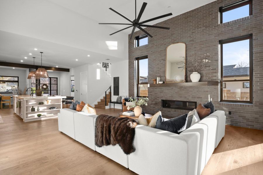 Living room featuring brick wall, a high ceiling, a brick fireplace, light wood-type flooring, and recessed lighting