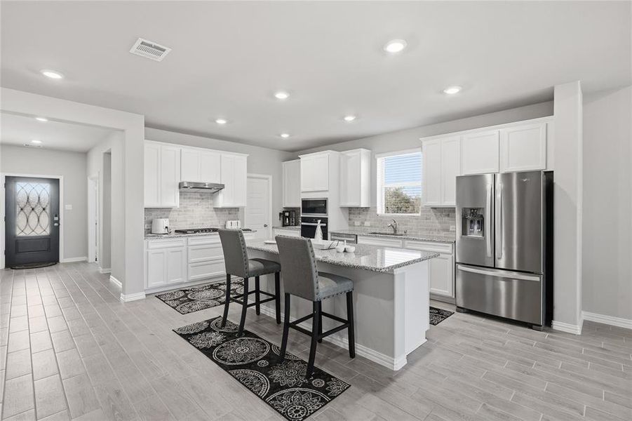 Open-concept kitchen featuring an island with seating, white shaker-style cabinetry, stainless steel appliances, and wood-finish flooring