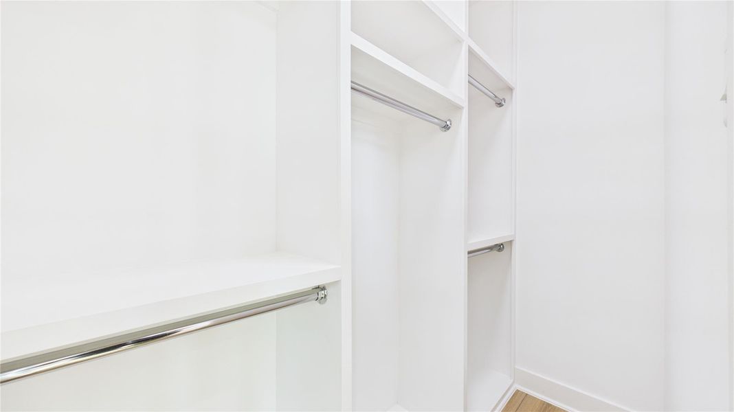 This photo shows a spacious, well-lit walk-in closet with white shelving and multiple hanging rods, perfect for organized storage.