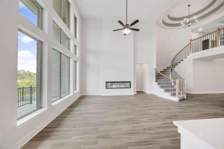Unfurnished living room featuring a glass covered fireplace, wood finish floors, ceiling fan, stairs, and a towering ceiling Unfurnished living room featuring a glass covered fireplace, wood finish floors, ceiling fan, stairs, and a towering ceiling