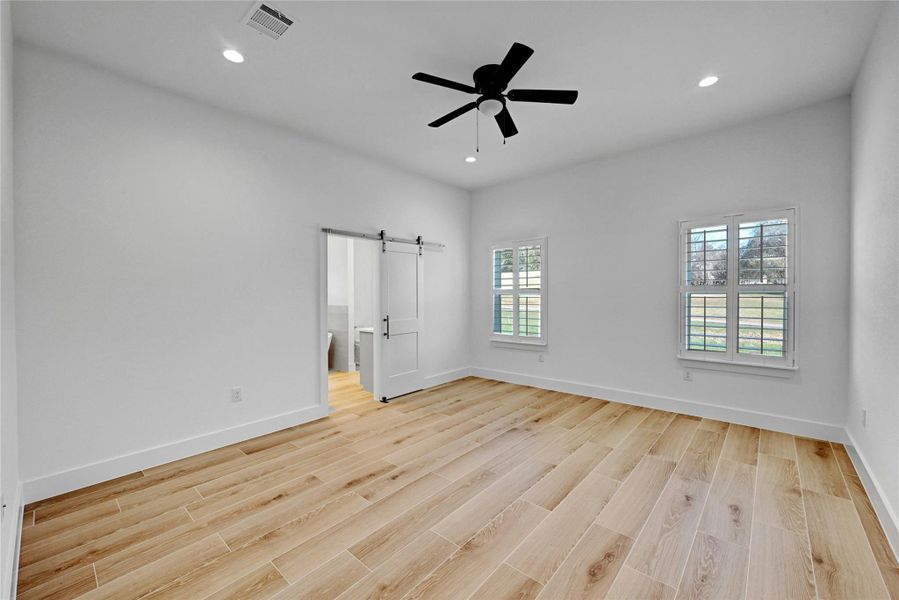 Beautiful primary bedroom showcasing the natural lighting and barn door leading to the primary bathroom.