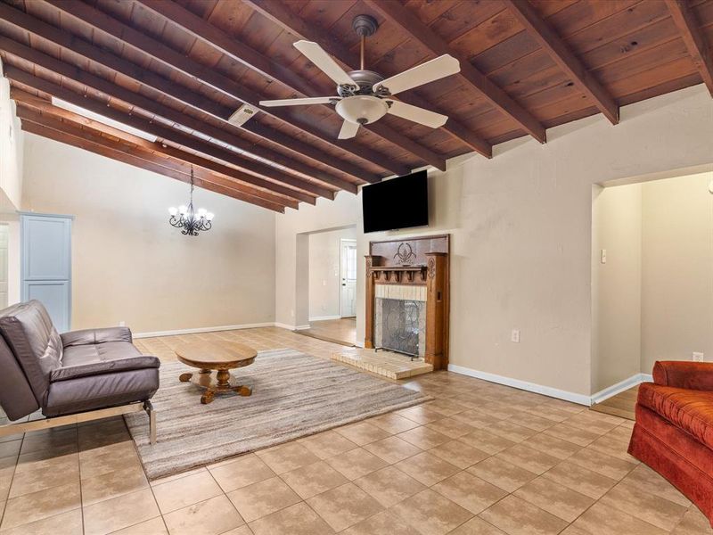 Living area featuring wooden ceiling, a brick fireplace, light tile patterned flooring, ceiling fan, and a chandelier Living area featuring wooden ceiling, a brick fireplace, light tile patterned flooring, ceiling fan, and a chandelier
