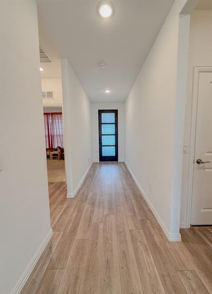 Hallway featuring baseboards, visible vents, and light wood finished floors