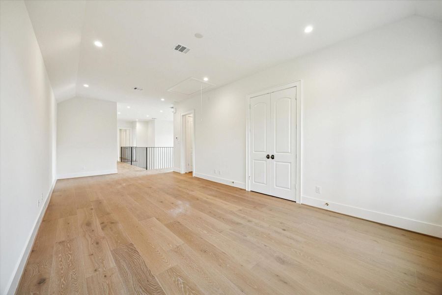 Spacious upstairs game room with wide-plank floors, recessed lighting, and open rail views to the foyer.