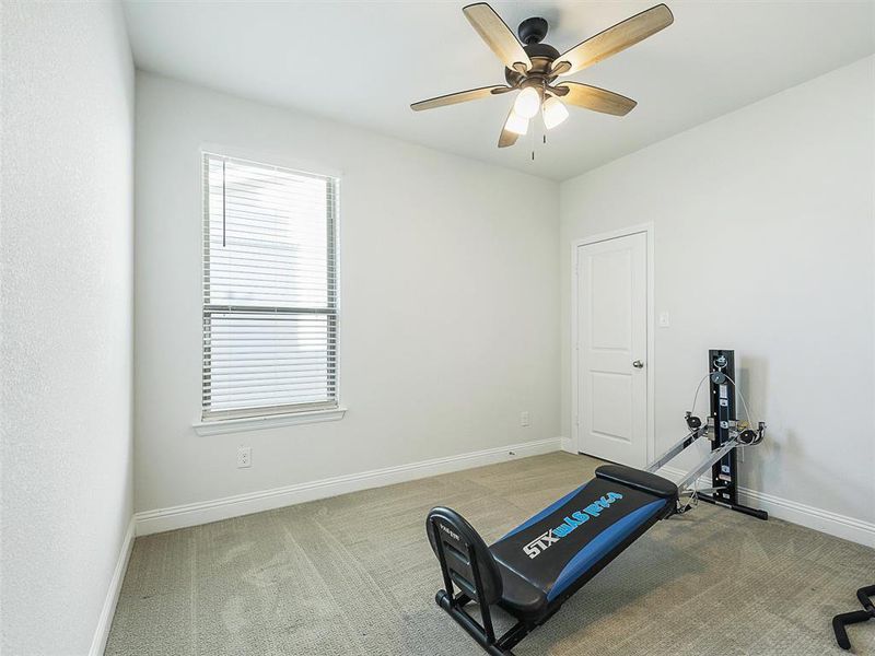 Bedroom currently used as workout room with light carpet and ceiling fan