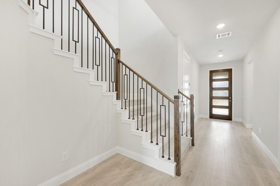 Entryway with staircase featuring wood and iron railing, light hardwood floors, and wood front door with glass panels