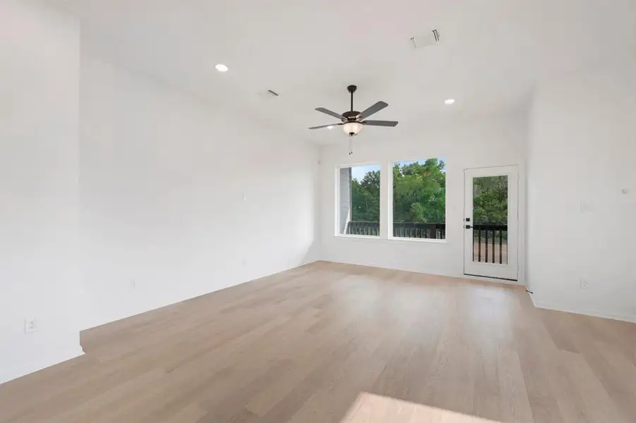 Spacious room featuring light wood-finish flooring, recessed lighting, and a ceiling fan with light kit