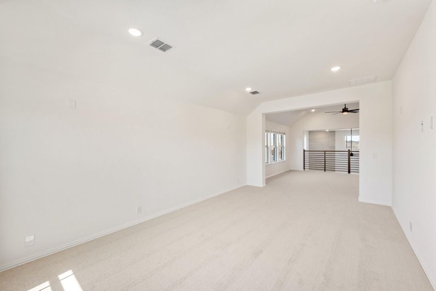 Empty upstairs loft with carpet flooring, white walls, arched opening, and metal railing overlooking lower level