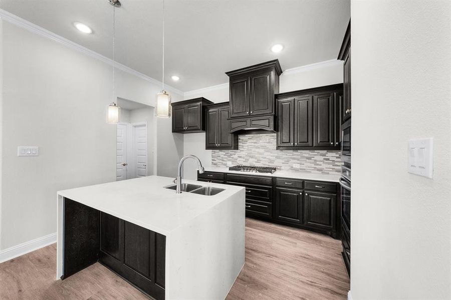 Kitchen with tasteful backsplash, ornamental molding, dark cabinets, light wood-style floors, and a center island with sink Kitchen with tasteful backsplash, ornamental molding, dark cabinets, light wood-style floors, and a center island with sink