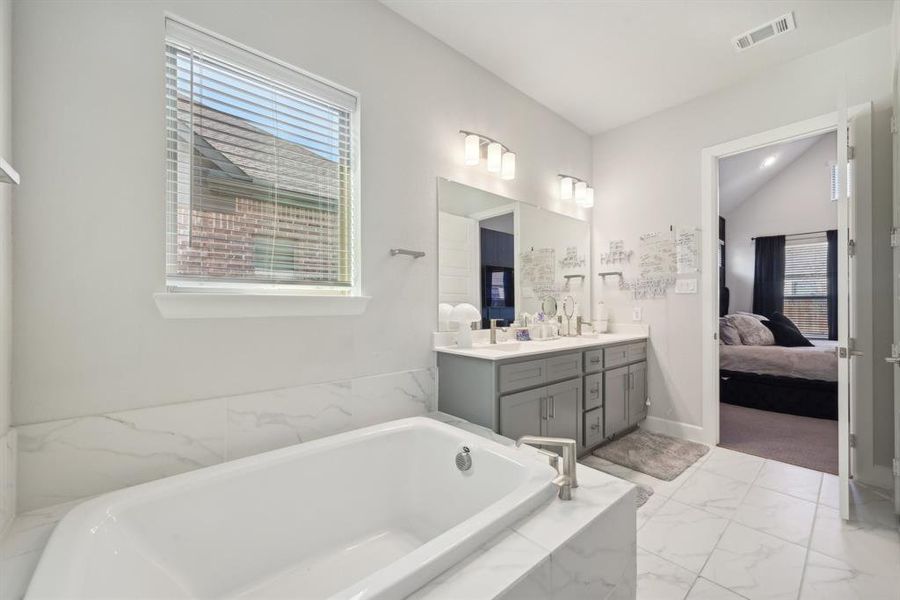 Bathroom featuring vanity, a relaxing tiled tub, and lofted ceiling