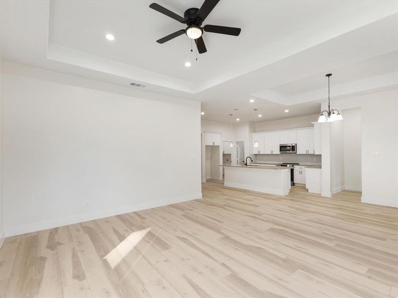 Unfurnished living room with recessed lighting, a raised ceiling, light wood-style floors, a ceiling fan, and a chandelier