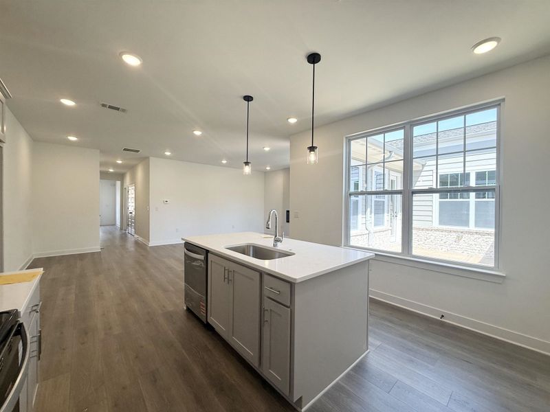 Kitchen featuring dark wood finished floors, a center island with sink, decorative light fixtures, light stone countertops, and black range oven