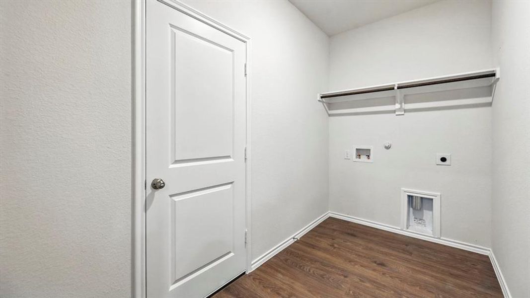 Dedicated laundry area featuring wood-finish flooring, crisp white walls, a two-panel interior door, and a built-in shelving unit with a hanging rod