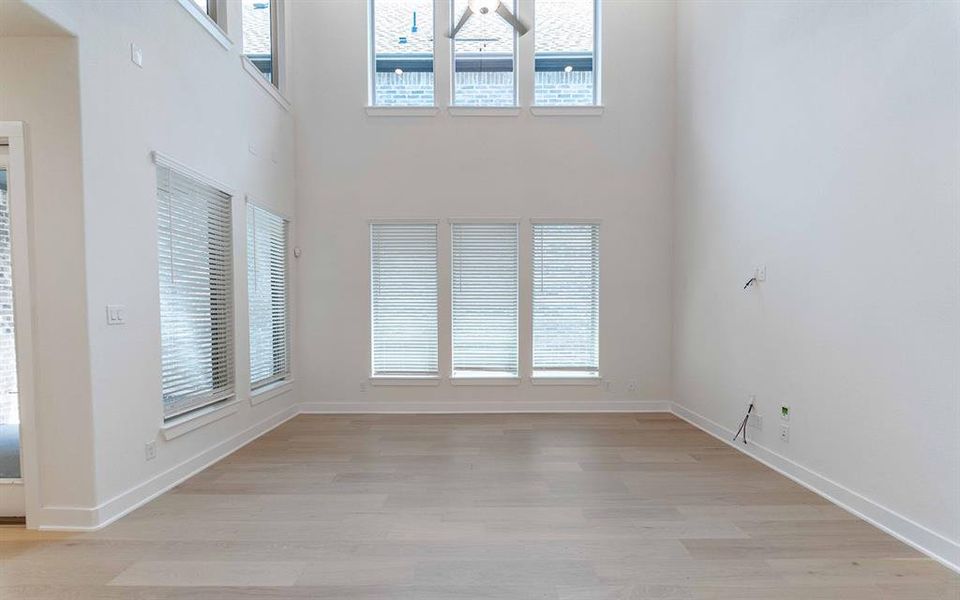 Two-story living area featuring wood-finish flooring, tall ceilings, and multiple windows with blinds