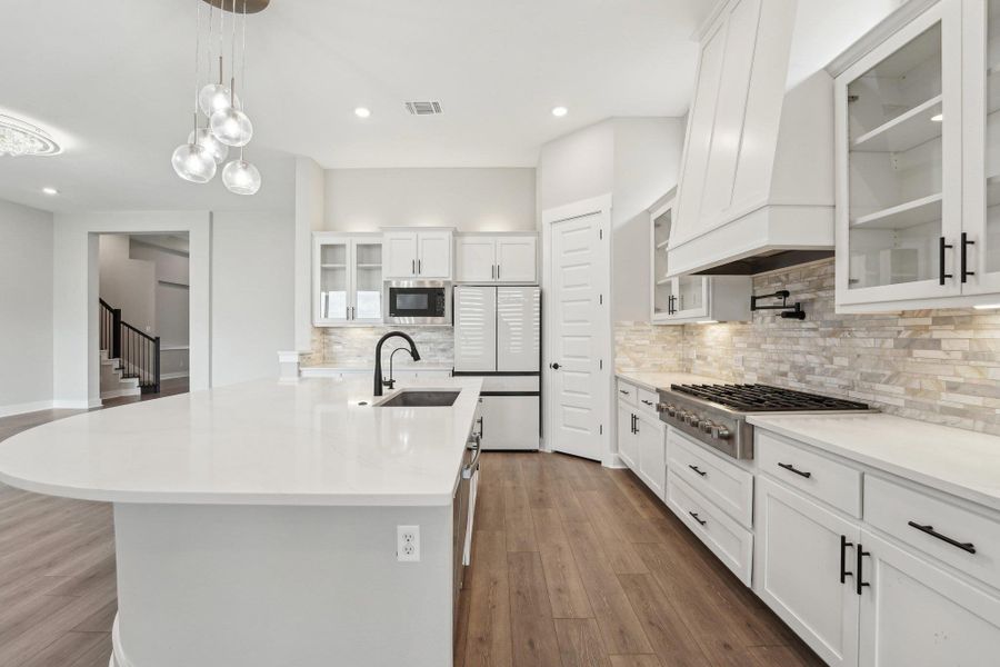 Kitchen featuring stainless steel gas stovetop, built in microwave, a sink, freestanding refrigerator, and custom exhaust hood Kitchen featuring stainless steel gas stovetop, built in microwave, a sink, freestanding refrigerator, and custom exhaust hood