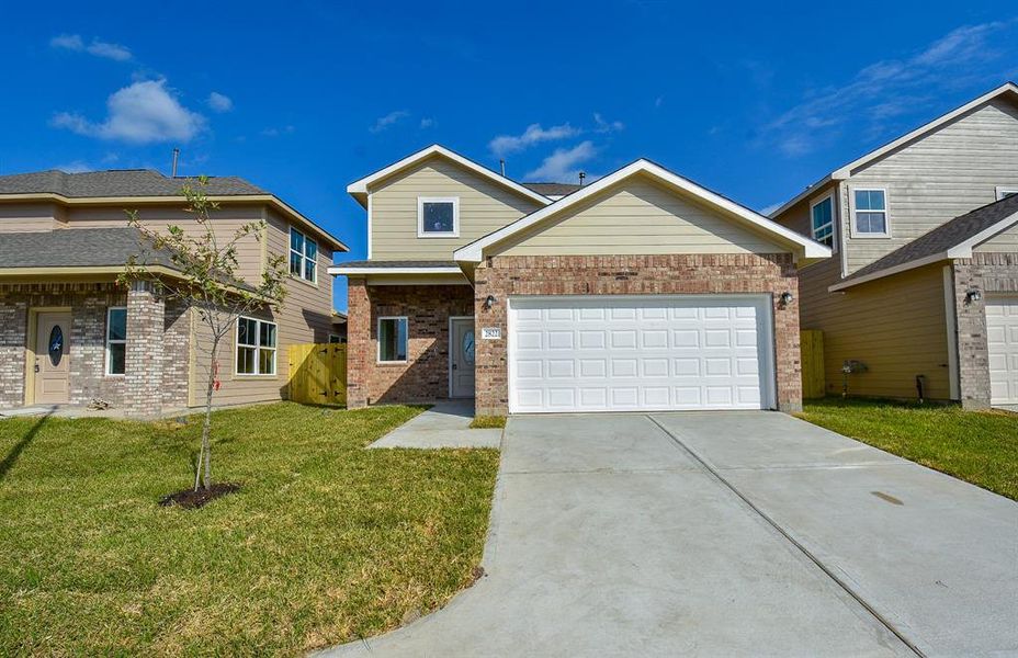 A new suburban house with a two-car garage, brick facade, small tree in front yard, and a clear blue sky.