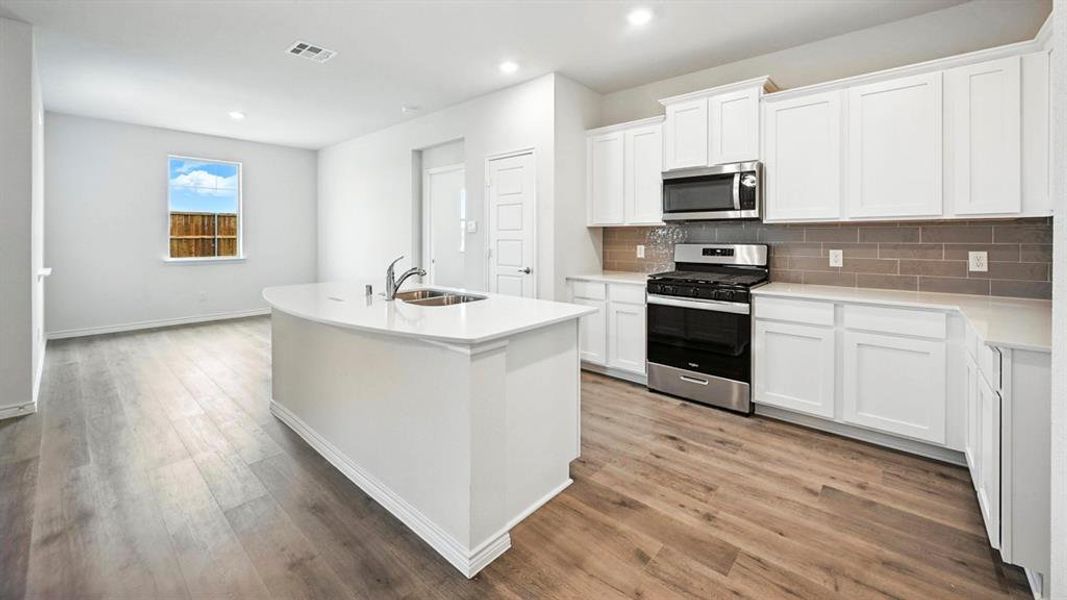 Spacious kitchen featuring white cabinetry, a large island with an integrated sink, stainless steel appliances, and wood-finish flooring