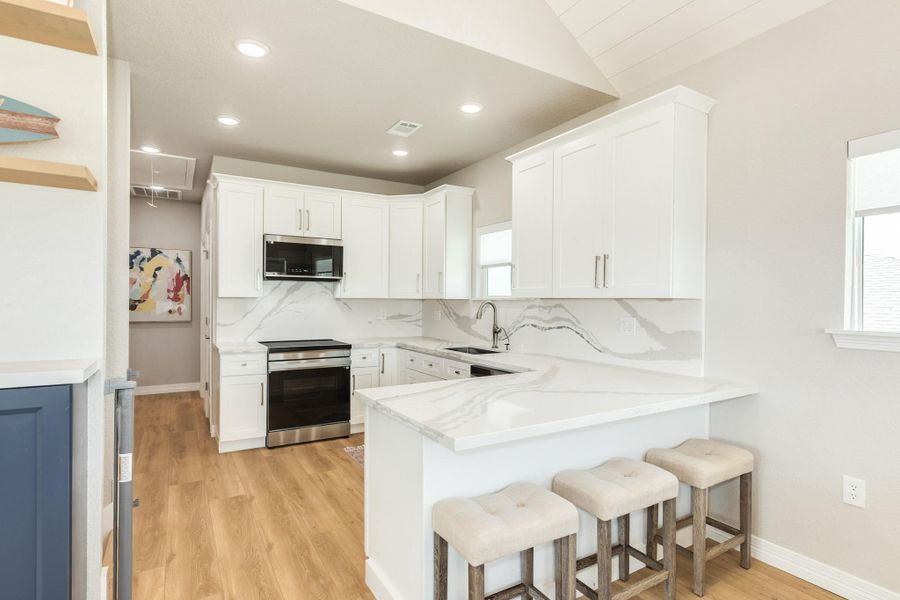 Contemporary kitchen showcases quartz countertops, custom white cabinetry, stainless steel appliances, a spacious peninsula with seating, and a striking full-height backsplash.