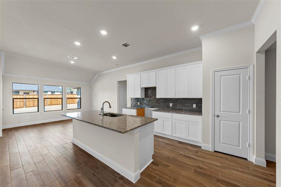Kitchen with white cabinetry, dark stone countertops, an island with sink, recessed lighting, and backsplash