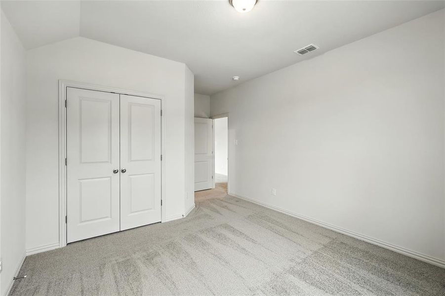 Unfurnished bedroom featuring light colored carpet, a closet, and vaulted ceiling