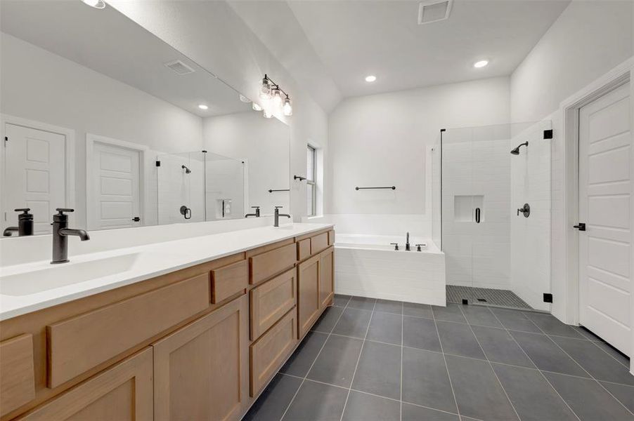 Full bath featuring a shower stall, double vanity, a bath, and dark tile patterned flooring