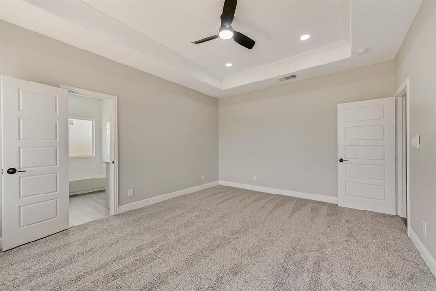 Unfurnished bedroom with ceiling fan, light colored carpet, and a tray ceiling