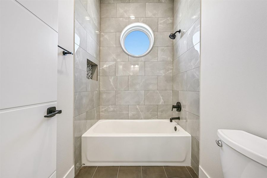 A circular accent window fills the bathroom with soft natural light while the tub and shower combination create a spa like setting. Neutral finishes and thoughtful design bring warmth and comfort.