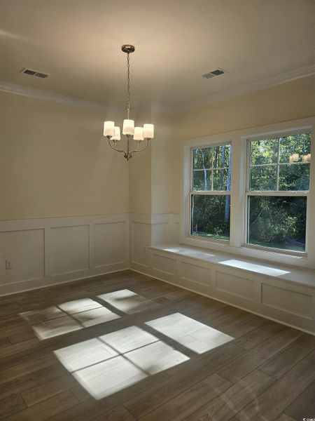 Unfurnished dining area featuring a decorative wall, crown molding, a wainscoted wall, a chandelier, and dark wood finished floors Unfurnished dining area featuring a decorative wall, crown molding, a wainscoted wall, a chandelier, and dark wood finished floors