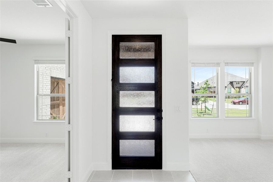 Dark wood front door with five frosted glass panels in a bright white entryway with tile floors