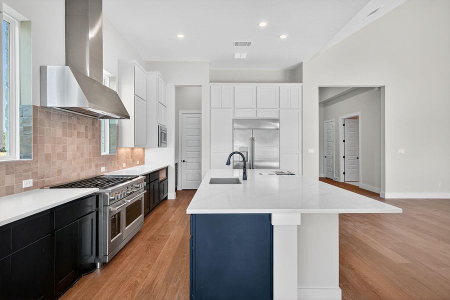 Kitchen with light wood-style floors, wall chimney exhaust hood, built in appliances, light stone counters, and white cabinets Kitchen with light wood-style floors, wall chimney exhaust hood, built in appliances, light stone counters, and white cabinets