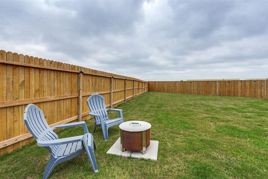 A spacious backyard enclosed by a tall privacy fence, featuring a cozy fire pit area.