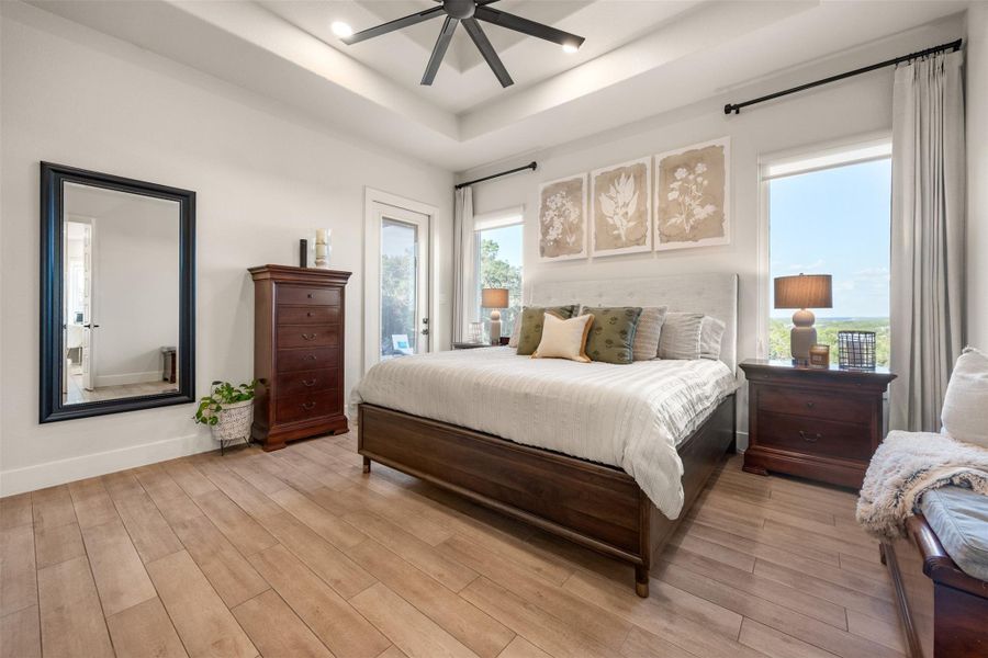 Bedroom featuring ceiling fan, access to exterior, a raised ceiling, and light hardwood / wood-style floors Bedroom featuring ceiling fan, access to exterior, a raised ceiling, and light hardwood / wood-style floors