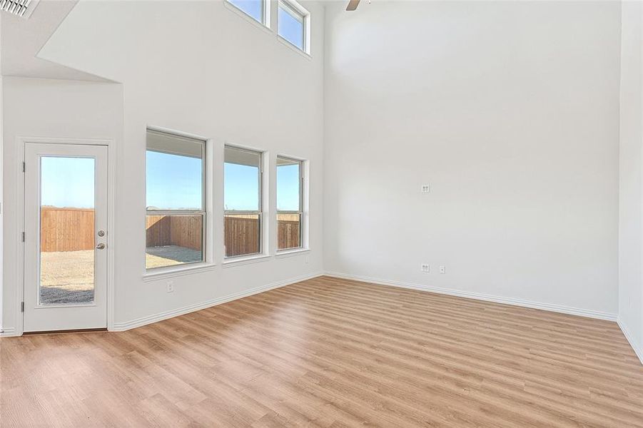 Empty room with light wood finished floors, a high ceiling, and ceiling fan