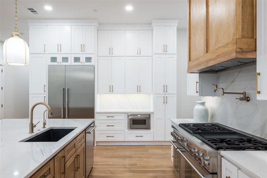 Kitchen with decorative backsplash, white cabinetry, sink, light wood-type flooring, and high quality appliances