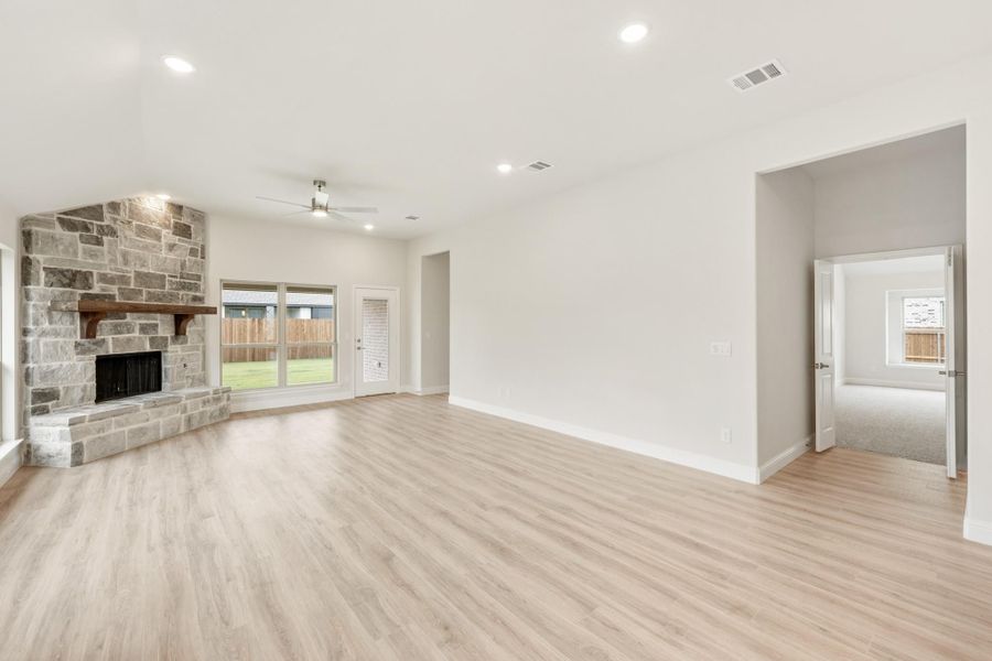 Open living room with stone fireplace, ceiling fan, and light hardwood floors