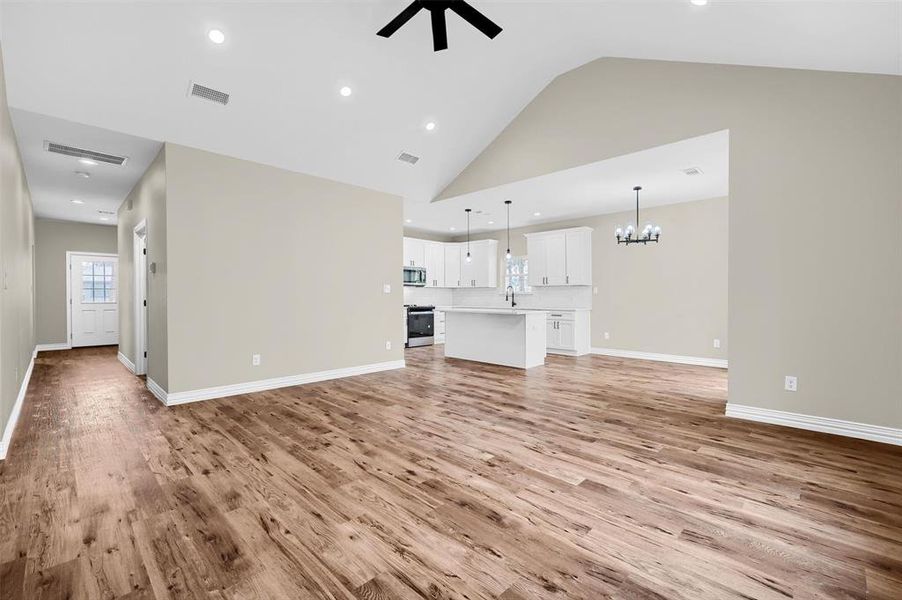 Unfurnished living room featuring light hardwood / wood-style flooring, high vaulted ceiling, ceiling fan with notable chandelier, and sink