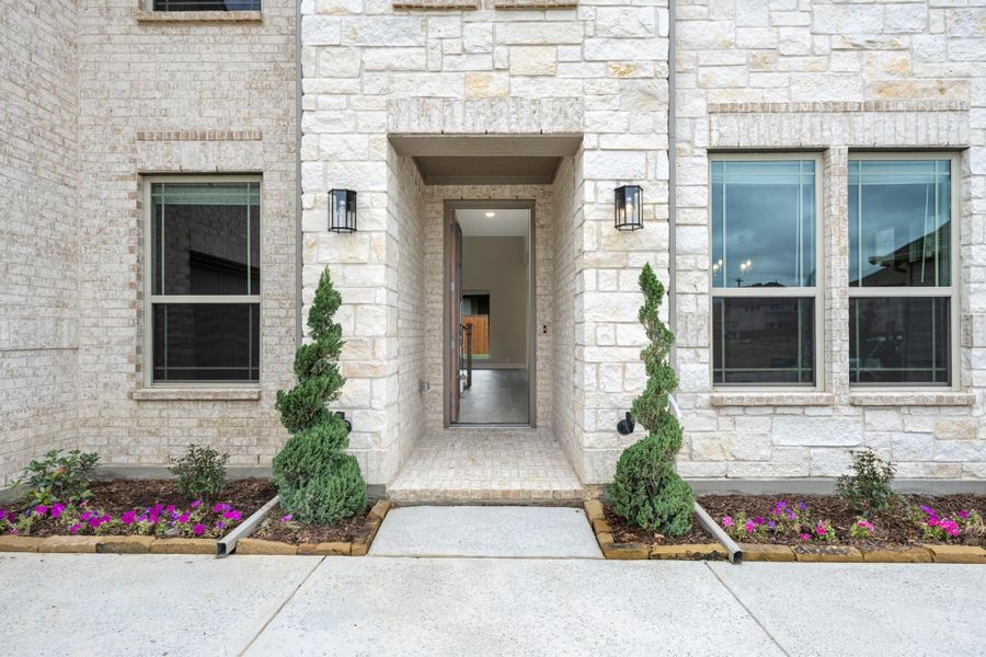 Home entrance with open front door, light stone exterior, wall sconces, and spiral topiaries flanking the entry