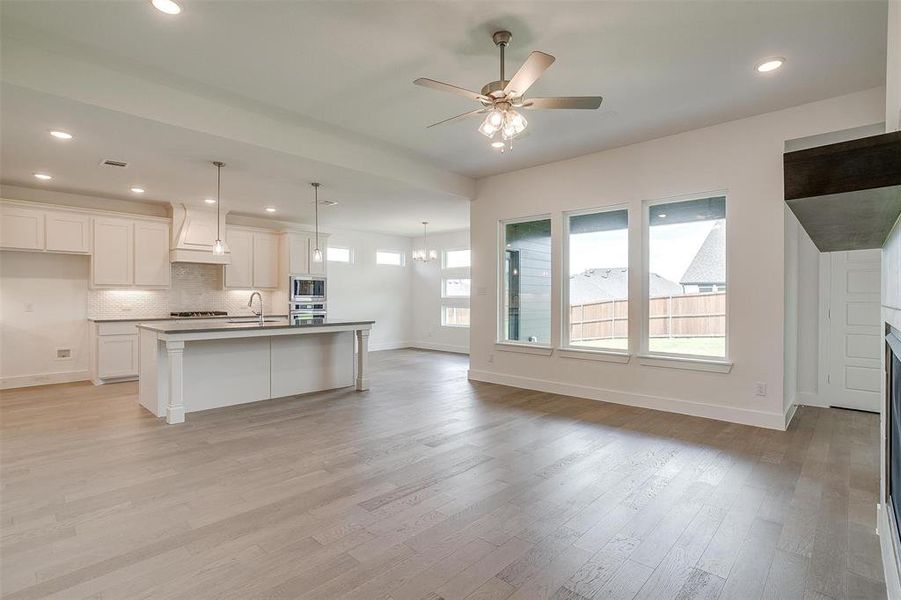 Kitchen with decorative light fixtures, tasteful backsplash, light wood-type flooring, and a kitchen island with sink