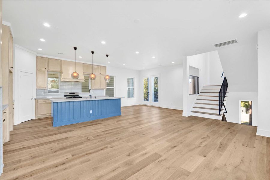 Second-floor main living and kitchen area with abundant natural light, high ceilings, engineered wood floors, custom built-ins, and a stunning custom fireplace as the focal point. Features an oversized island with Taj Mahal quartzite countertops and integrated appliances.