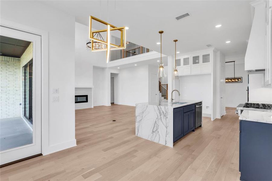 Kitchen featuring white cabinets, a glass covered fireplace, light stone counters, light wood-type flooring, and recessed lighting